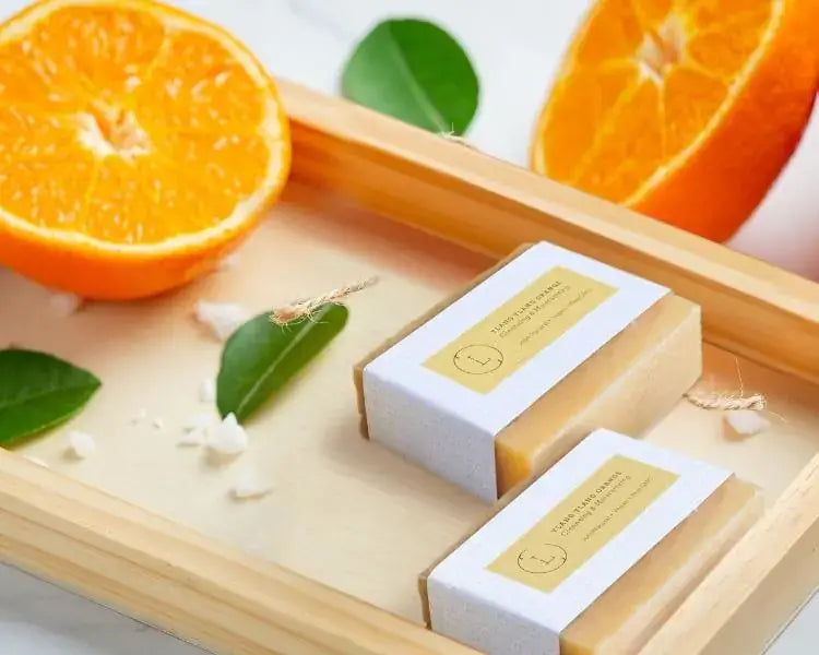 Yalng Yalng Orange Natural Soap Bar with fresh orange slices and green leaves on a wooden tray.
