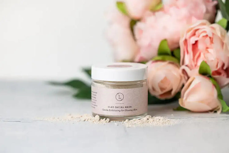 Clay facial mask jar surrounded by peony flowers, offering gentle exfoliation for glowing skin.