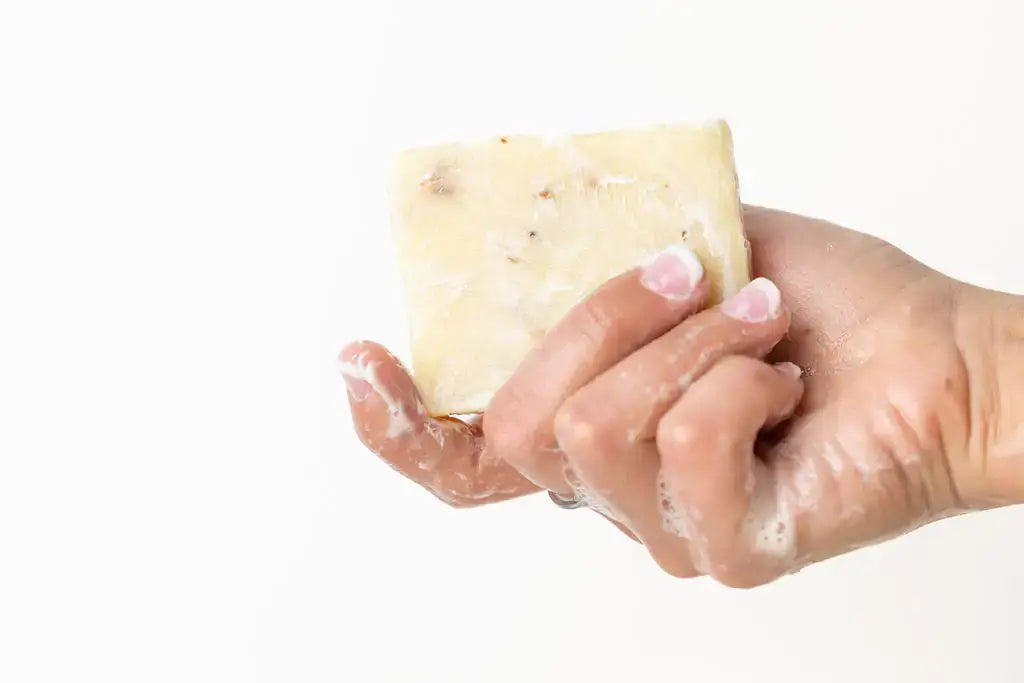 Hand holding a natural lemongrass soap bar, showcasing a creamy lather on a gentle hand.