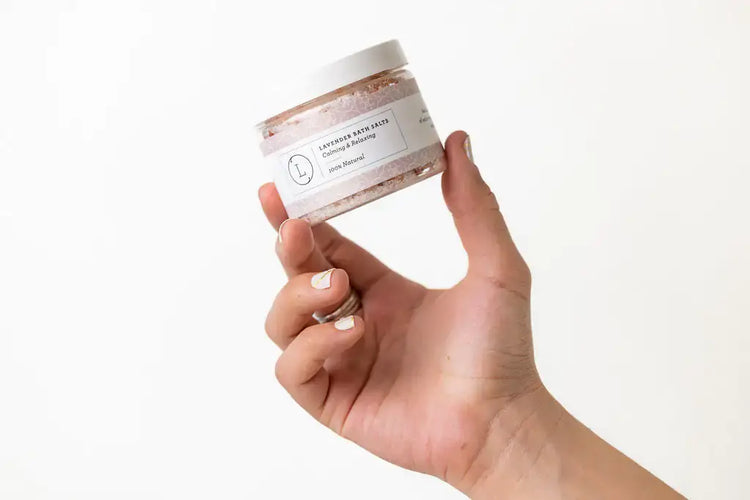 Person holding a jar of lavender sea salts from the Lavender Luxury Gift Box for self-care.