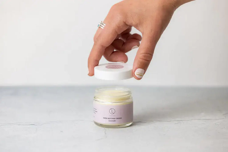 Hand opening a lavender infused shea butter cream jar, perfect for self-care and gifting.
