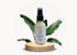 Organic facial moisturizer bottle on wooden pedestal surrounded by green leaves, promoting natural skincare.
