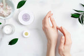 Hands applying lavender shea butter body cream with natural skincare products on a marble surface.