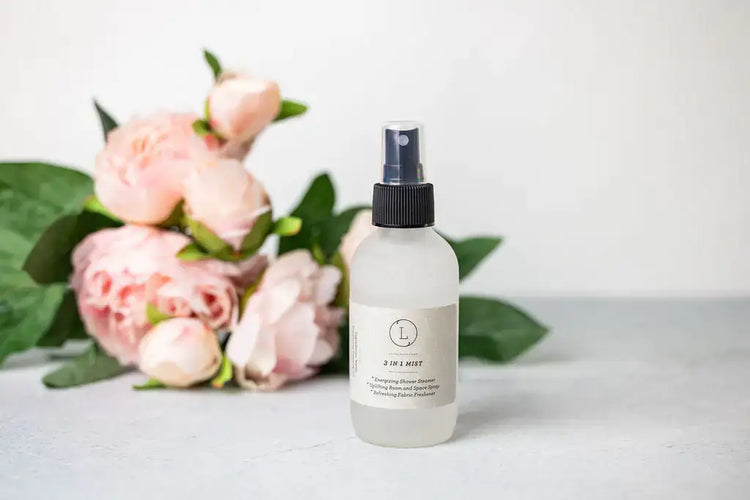 Soul Touch Massaging Set spray bottle next to pink peonies, perfect for skincare and self-care routines.