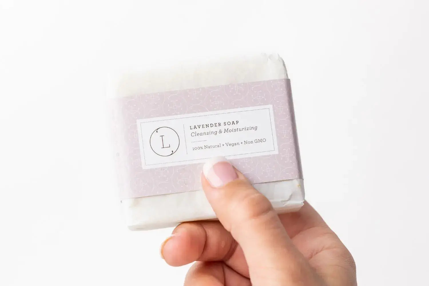 Hand holding a lavender soap bar labeled for cleansing and moisturizing, 100% natural and vegan.