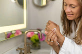 Woman applying Lavender Shea Butter Body Cream in a bathroom, showcasing hydration and skincare routine.